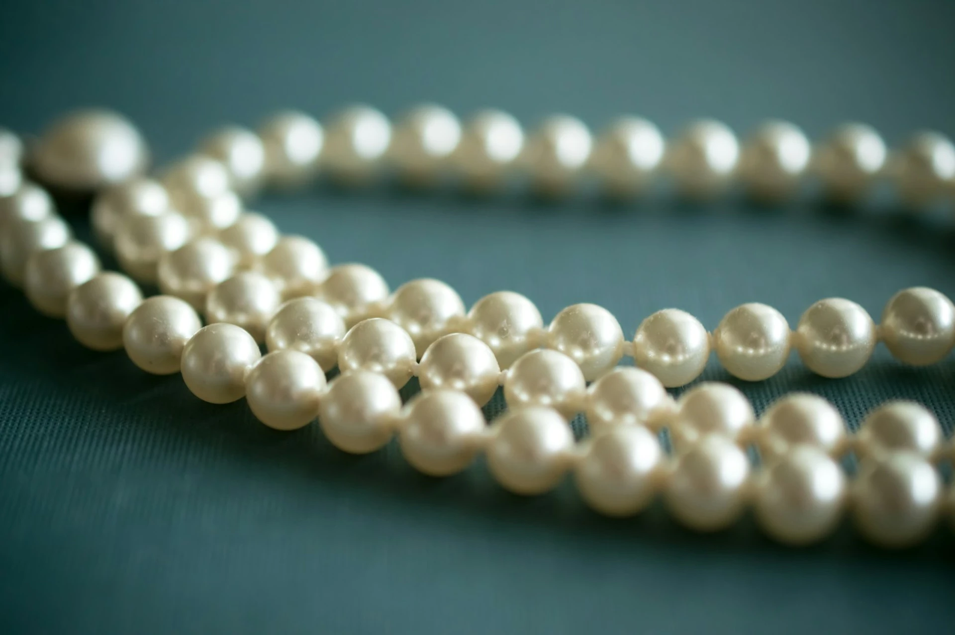Strand of white pearls resting on deep teal fabric