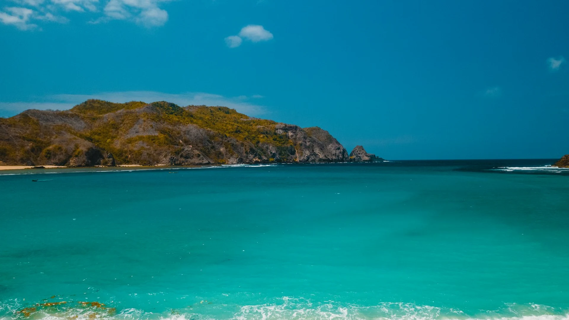 Clear turquoise bay below green hills on the Lombok coast