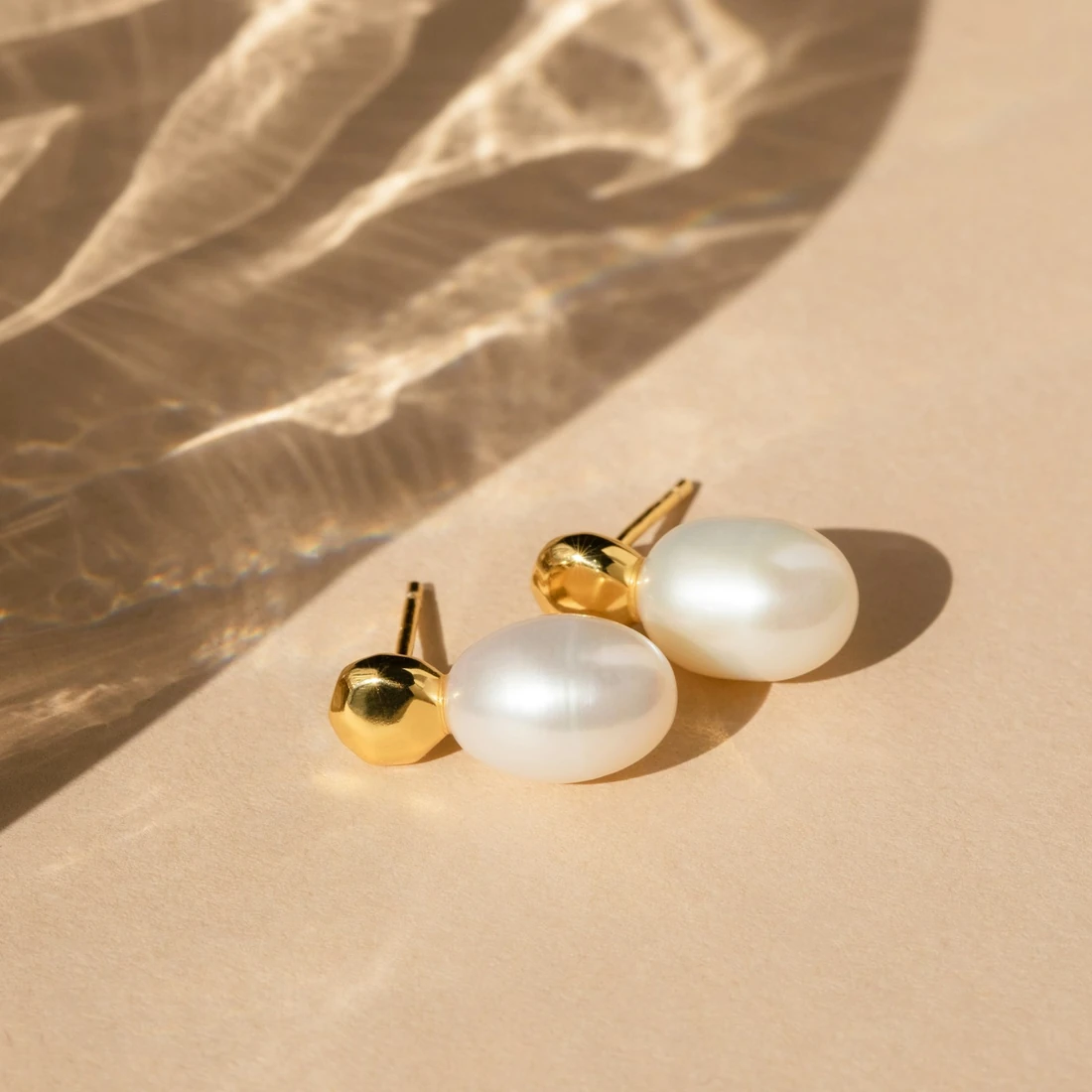 Pearl stud earrings on sand-coloured stone in sunlight