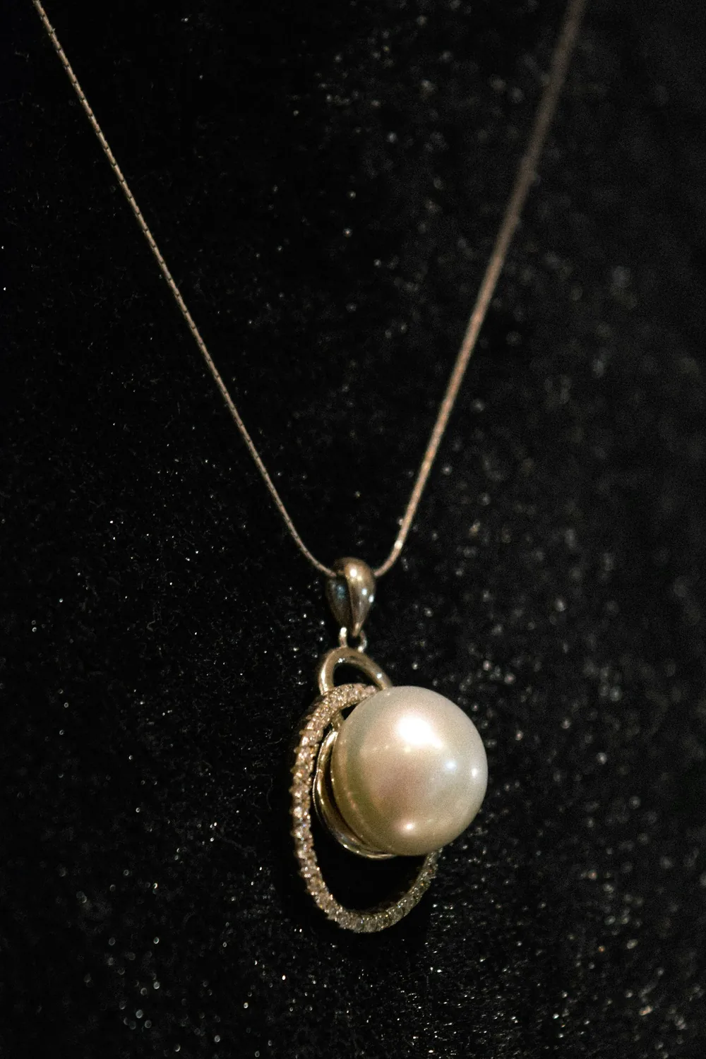 Single white pearl pendant on a fine chain against black