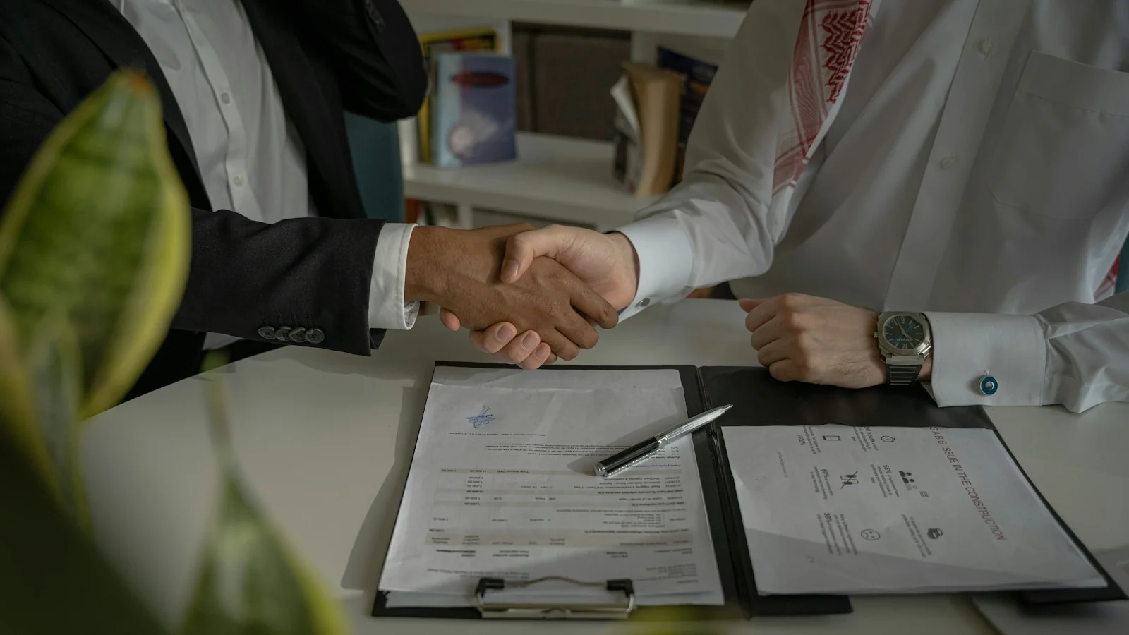 Business partners shaking hands over signed documents